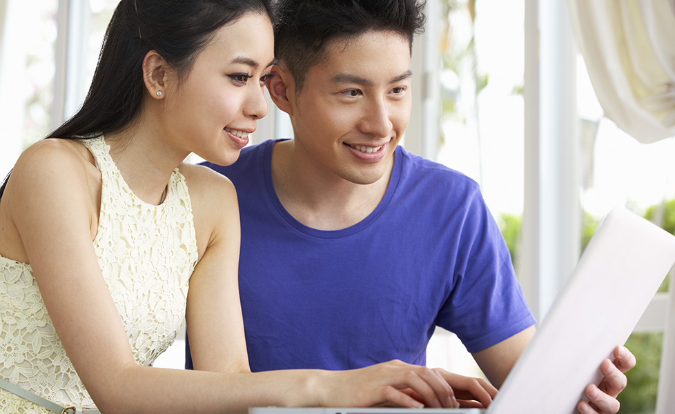 Young Chinese Couple Sitting At Desk And Using Laptop figuring out how to use paypal